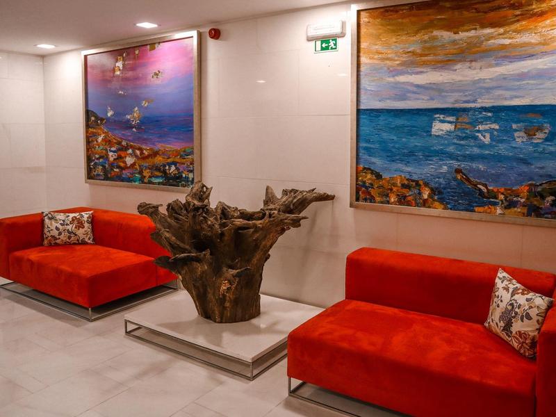 Roter Samtsessel mit gemusterten Kissen, abstrakte Gemälde an weißen Wänden und Holzskulptur.