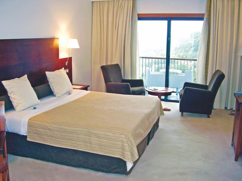 Ein helles Hotelzimmer mit großem Doppelbett, zwei Sesseln, kleinem Tisch und Balkon.