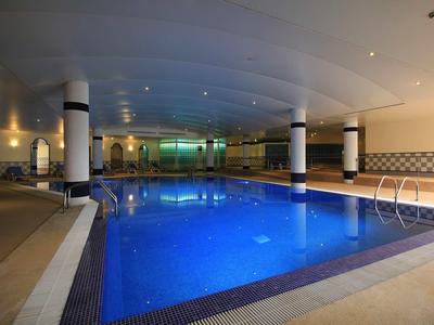 Vnitřní bazén s modře osvětlenou vodou, bílými sloupy a odpočinkovými zónami