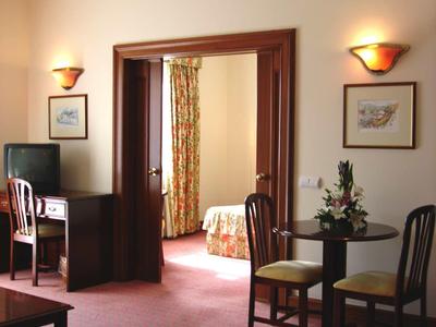 Pokoj s kobercem, dvěma židlemi, malým stolem a výhledem do další místnosti.