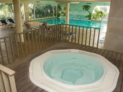 Vírivka v hotelovém wellness s bazénem a lehátky v pozadí.