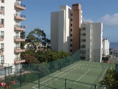 Tennisplatz mit Netz zwischen mehrstöckigen Hotelgebäuden und Blick auf den Ozean.