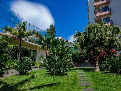 Zelená zahrada s palmami a cestou před hotelovou budovou pod modrou oblohou.