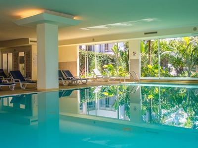 Vnitřní bazén s lehátky a velkými okny s výhledem na tropické rostliny.