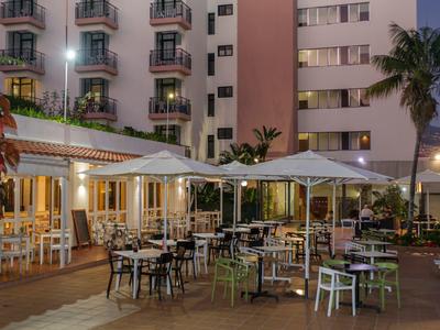 Venkovní prostor hotelu s terasou, stoly a velkými slunečníky za soumraku.