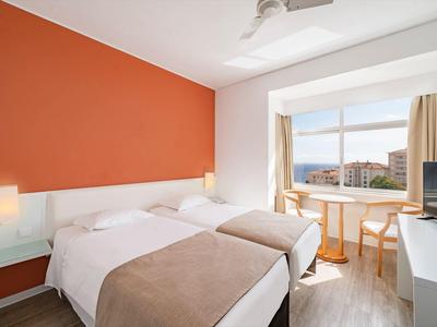 Hotelový pokoj se dvěma jednolůžky, oranžovou zdí a balkonem s výhledem na město.