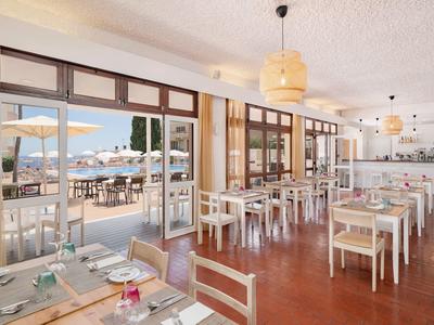 Světlá restaurace s bílými stoly a výhledem na slunnou terasu a moře.