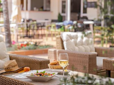 Pohodlná venkovní hotelová terasa s občerstvením a sklenkou bílého vína na stole.