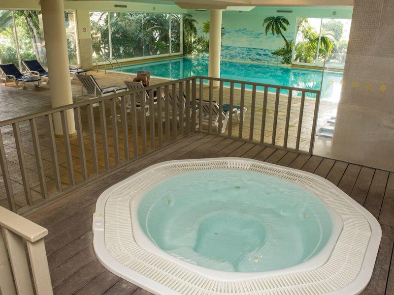 Vírivka v hotelovém wellness s bazénem a lehátky v pozadí.