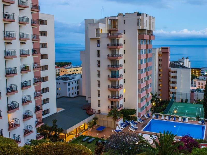 Hotelové budovy s balkony, bazénem a výhledem na moře za denního světla.