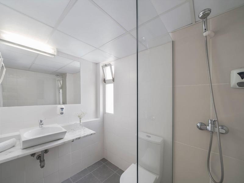 Světlá, moderní koupelna s umyvadlem, toaletou, zrcadlem a sprchou s skleněnou přepážkou.