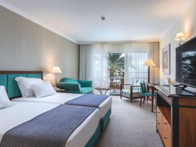 Modern eingerichtetes Hotelzimmer mit Doppelbett, Sitzecke und Balkon mit Pflanzenblick.