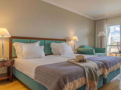 Modernes Hotelzimmer mit zwei Einzelbetten und Sitzbereich neben großem Fenster.