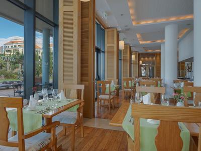 Modernes Restaurant mit Holzmöbeln und Blick auf Hotelgebäude durch große Fenster.