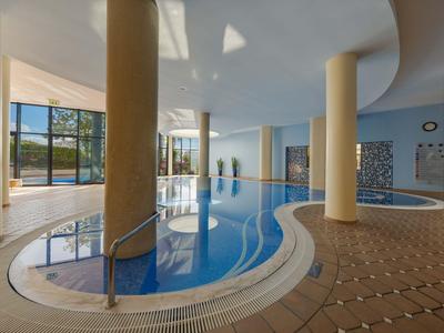 Innenpoolbereich mit Säulen, beigen Fliesen und großen Fenstern in einem Hotel.