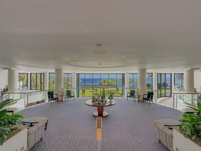 Weitläufige Hotellobby mit großen Fenstern und Blick auf Garten und Meer.