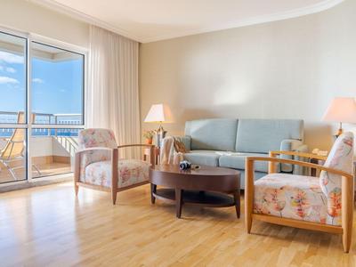 Helles Wohnzimmer mit Holzfußboden, blauen Sofa, zwei Sesseln und Balkonaussicht aufs Meer.