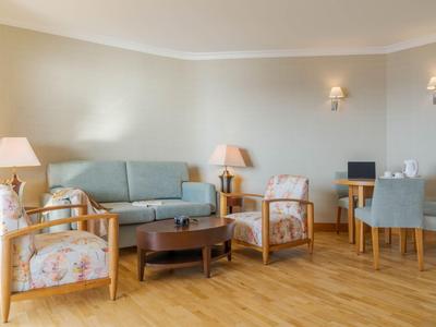 Helles Hotelzimmer mit Holzfußboden, blauem Sofa, Blumenstühlen und kleinem Arbeitsplatz.