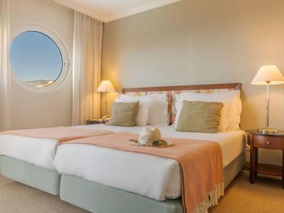 Helles Hotelzimmer mit zwei Einzelbetten, runden Fenster und warmem Licht.