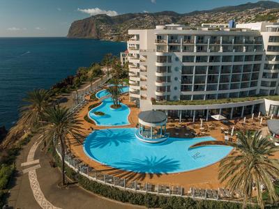 Modernes Hotel mit geschwungenem Pool und Meerblick, umgeben von Palmen.