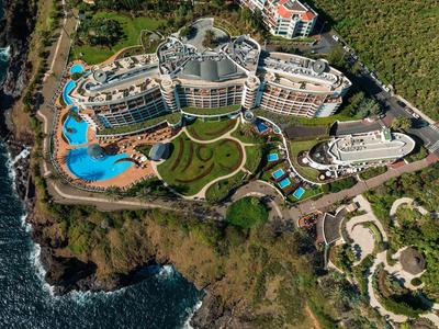 Luftaufnahme eines Hotels an der Küste mit mehreren Pools und grünen Gartenanlagen.