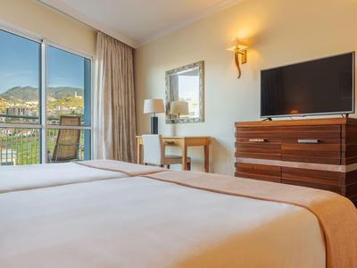 Modernes Hotelzimmer mit Bett, Schreibtisch, Fernseher und Bergblick durch große Fenster.