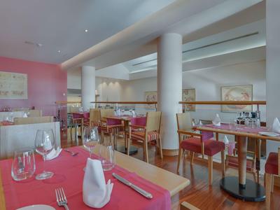 Moderner Restaurantbereich mit Holztischen, roten Tischdecken und weiß gedeckten Gläsern.