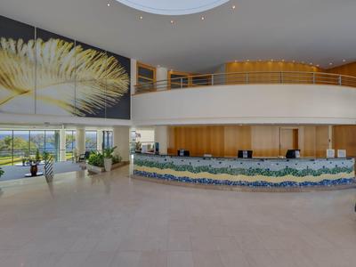 Helle Hotellobby mit großer Rezeption, Kunst an der Wand und Fenster mit Meerblick.