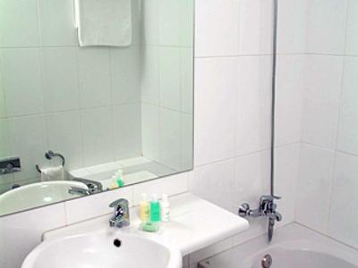 Kleine weiße Badezimmerecke mit Rundwaschbecken, Spiegel, Badewanne und Duschkopf.