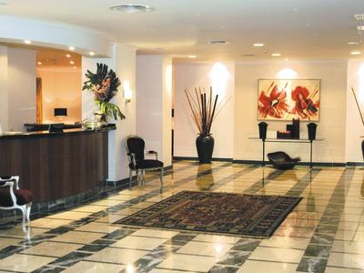 Elegante Hotellobby mit dunklem Empfangstresen, großen Vasen und beigem Marmorboden.