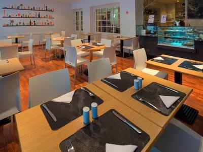 Modernes Restaurant mit Holzboden, schwarzen Placemats und weißem Mobiliar, hell und einladend.