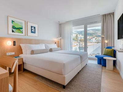 Modern hotelkamer met tweepersoonsbed, balkon en uitzicht op bergen en stad.