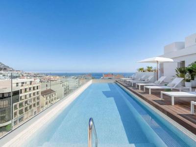 Piscina infinita en terraza en la azotea con vistas a la ciudad y el mar bajo un cielo despejado.