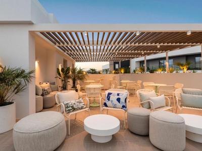 Moderna terraza de hotel con asientos cómodos y plantas bajo una pérgola de madera.