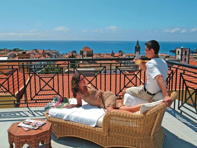 Uomo seduto su terrazza con mobili in vimini con vista sulla città e sul mare