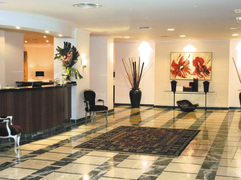 Luminosa hall dell'hotel con reception, sedie e piante decorative in grandi vasi.