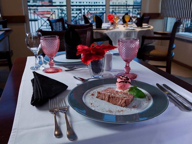 Ristorante elegante con tavolo apparecchiato, bicchieri rosa e dessert decorativo.