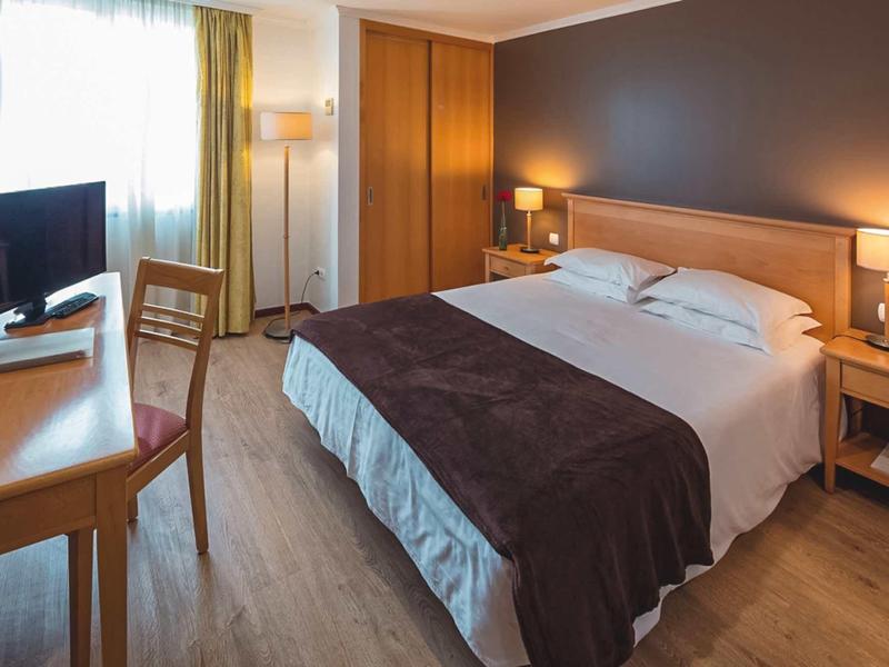 Camera d'hotel moderna con letto grande, scrivania, sedia e pavimento in legno