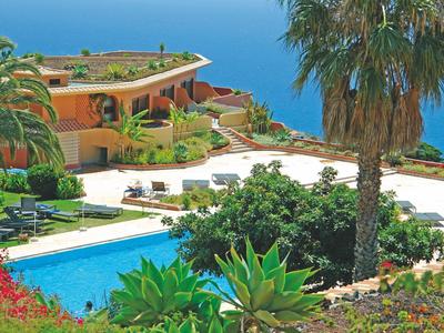 Moderner Wohnkomplex mit Pool, Palmen und üppigem Grün vor klarem blauem Himmel.