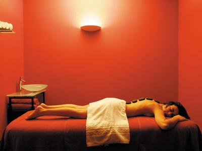 Entspannte Person liegt auf Massagebank in warmem, rot-orangefarbenem Raum mit sanfter Beleuchtung.