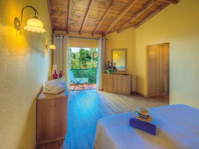 Helles Schlafzimmer mit Holzbalkendecke, gelben Wänden, Doppelbett und Zugang zum Garten.