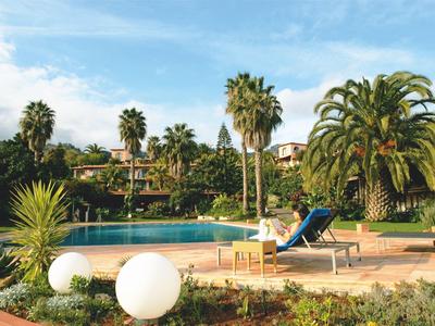 Schwimmbecken mit Liegestuhl, Palmen und Garten unter blauem Himmel.