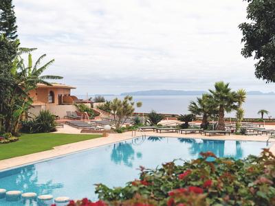 Großer blauer Pool mit Landschaft, Palmen und mediterranem Haus im Hintergrund.