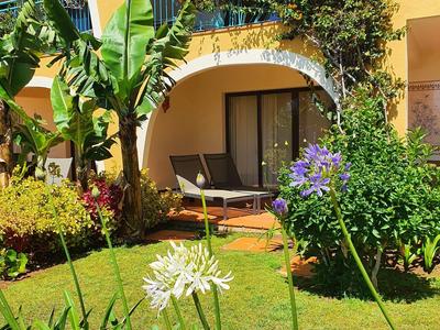 Grüner Garten mit blühenden Blumen vor einer gelben Hausfassade mit Terrasse und Sitzgelegenheiten.