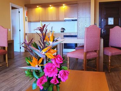 Blumenarrangement mit rosa Rosen und orangen Blüten auf einem Holztisch in Wohnzimmer mit Küchenzeile.