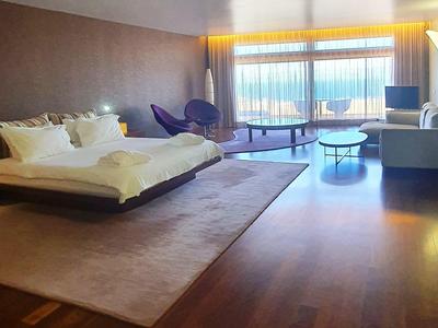 Großes Schlafzimmer mit Holzfußboden, Doppelbett, violetten Sesseln und Panoramafenster.
