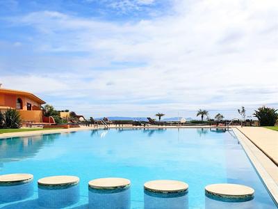 Großer blauer Pool mit runden Sitzflächen, Rand aus hellem Stein und klarem Himmel im Hintergrund.
