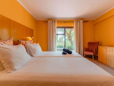 Przytulny pokój hotelowy z dwoma łóżkami, pomarańczowymi ścianami i widokiem na ogród.