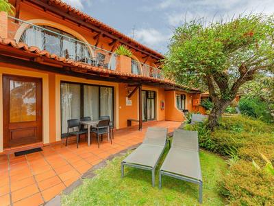 Dom z pomarańczową elewacją, tarasem z krzesłami i dwoma leżakami w ogrodzie.