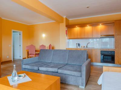 Przytulny salon z szarą sofą, drewnianymi meblami i otwartą kuchnią w ciepłych tonach.